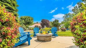 Een terras met een ronde vuurkorf en blauwe Adirondack stoelen.