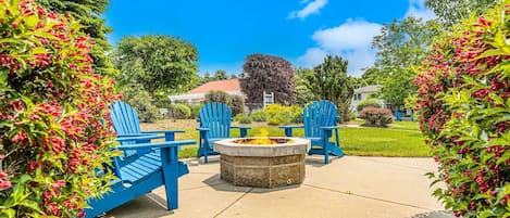 A patio area with a circular fire pit and blue Adirondack chairs.