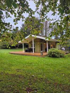 A covered outdoor seating area with tables and chairs, a wooden deck, and a small garden.