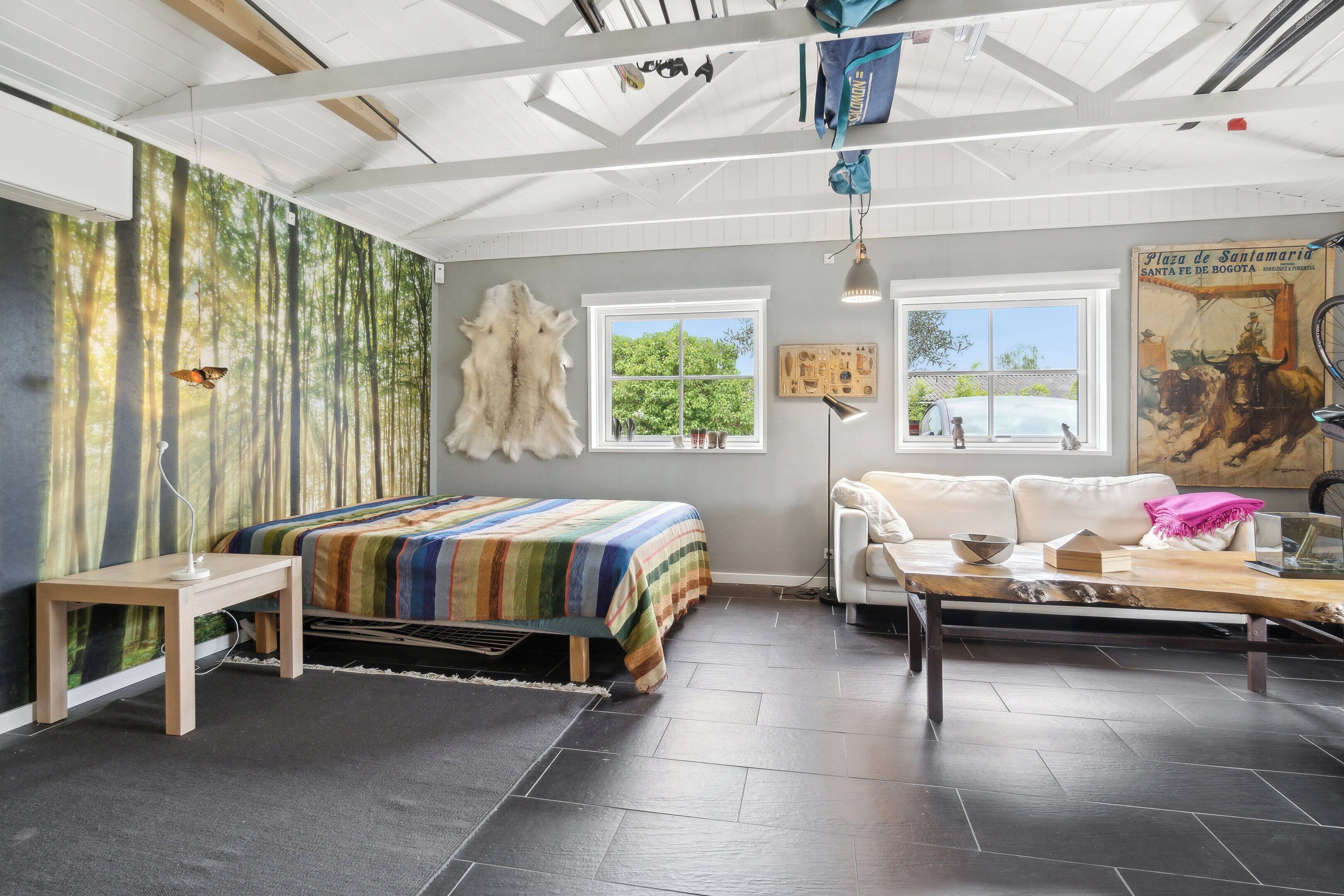 Una habitación con cama, sofá, mesa, ventana y una pared decorada con un mural de un bosque.