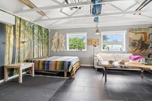 A room with a bed, a sofa, a table, a window, and a wall with a forest mural.