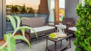 Un canapé et des fauteuils en osier sur une terrasse, avec une table et une lanterne.