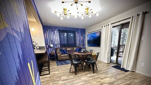 En moderne stue med en brun lædersofa, et spisebord med stole, et stort fjernsyn og en loftlampe.