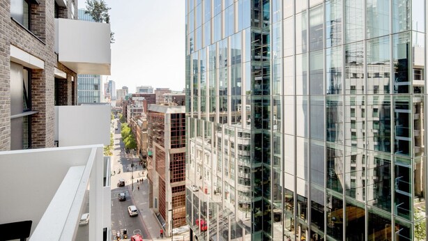 Un bâtiment moderne avec des fenêtres en verre réfléchissant, une façade en briques et une vue dégagée sur la rue en contrebas.