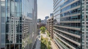 Un bâtiment urbain moderne aux façades vitrées réfléchissantes, doté d’une cour intérieure arborée et offrant une vue sur d’autres immeubles de grande hauteur en arrière-plan.