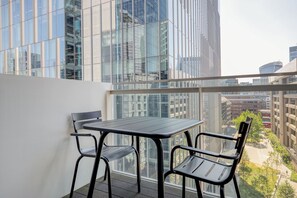 A balcony with a table and chairs, overlooking a cityscape with modern buildings.