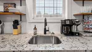 A kitchen with a stainless steel sink, a coffee maker, and shelves with dishes and utensils. - Springside Bourbon Getaway (Georgetown)