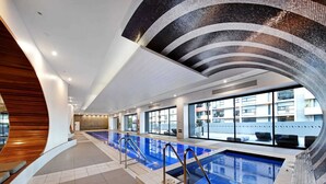 A modern indoor swimming pool with a curved ceiling and large windows overlooking a residential area.