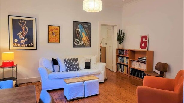 Een woonkamer met een witte bank, een boekenkast, een rode fauteuil en een groot nummer 6 op de muur.