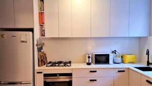 Een kleine keuken met witte kastjes, een inbouwoven, een magnetron, een broodrooster en een spoelbak.