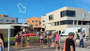 Een openbare buitenruimte met een modern gebouw, een overdekte zithoek en een waterpartij.