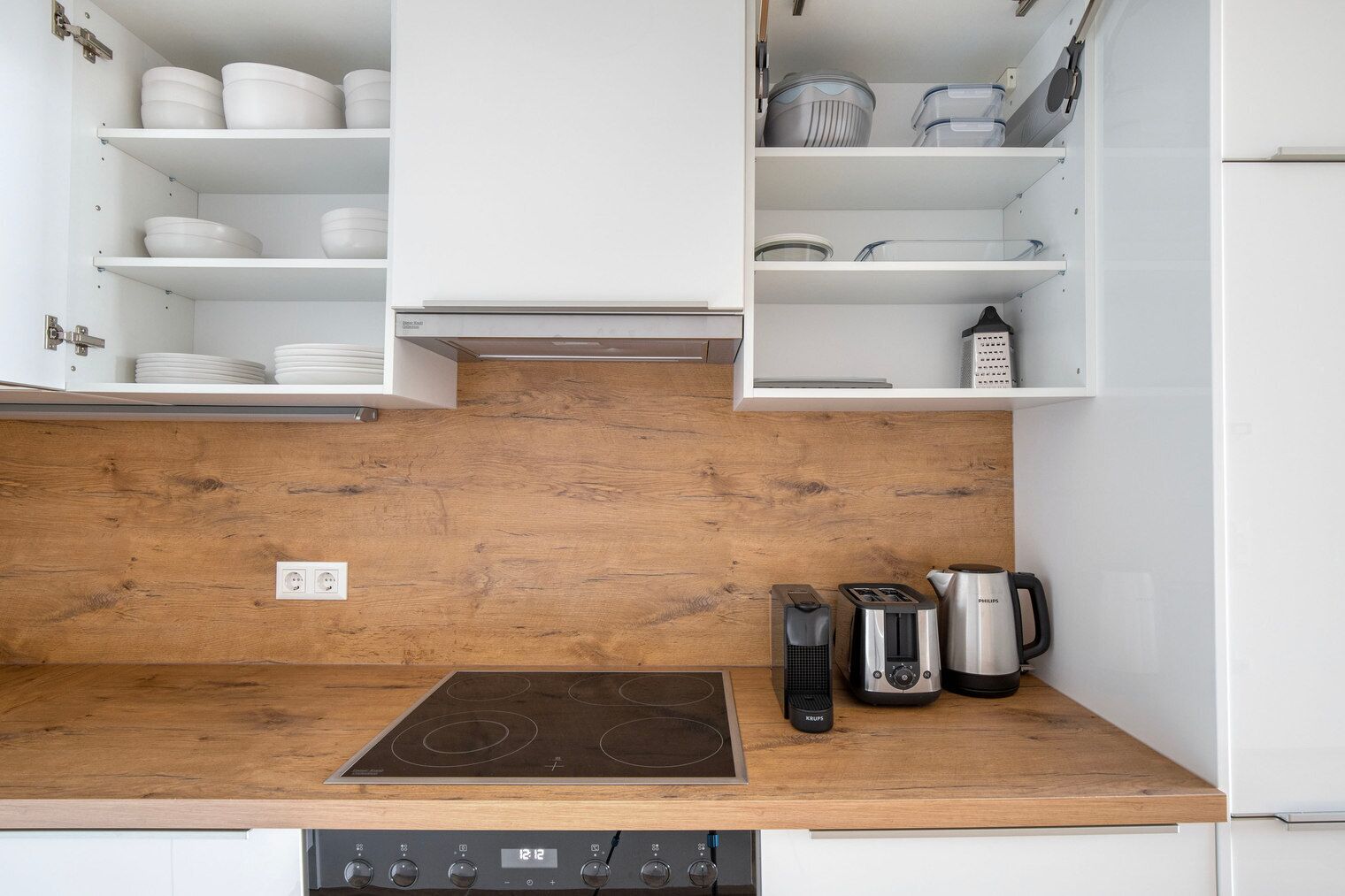 Een keuken met witte kastjes, een houten aanrecht, een inductiekookplaat, een koffiezetapparaat, een broodrooster en een waterkoker.