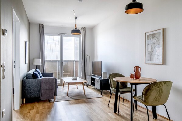 A modern living room with a sofa, a coffee table, a TV, and a dining area with chairs and a table. - Trendy Landstraße 1BR w/ Gym & Pool, nr Restaurants, by Blueground (Vienna)