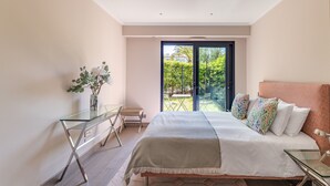 Un dormitorio con cama, escritorio de cristal, una silla y vistas al exterior.