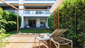 Un patio moderno al aire libre con terraza de madera, una mesa con una bebida y una silla de descanso.