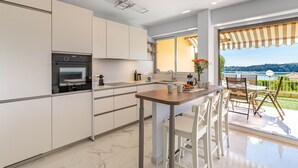 A modern kitchen with a built-in oven, white cabinets, and a large window overlooking a scenic view. - Flora Sur Mer 2 bedroom apartment (Villefranche-sur-Mer)