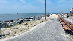 Ein Küstenweg mit Bänken, einem Holzpfosten und freiem Blick auf das Meer.