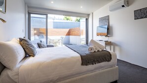Quarto de hotel moderno com uma cama grande, televisão, varanda com vista para a cidade e uma pequena mesa com cadeiras.