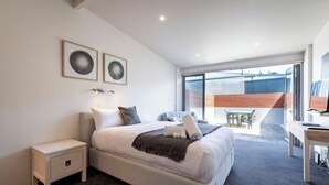 Quarto moderno com cama grande, mesa de cabeceira, escrivaninha e varanda com vista.