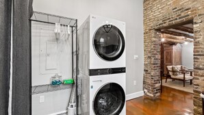 Une buanderie équipée de deux machines à laver et deux sèche-linge superposés, d’un étendoir métallique et d’un mur en briques.