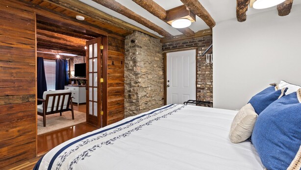 Une chambre avec un grand lit, des poutres en bois, un mur en pierre et un petit bureau avec une chaise.