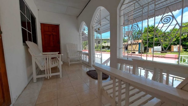 A covered porch with white chairs and a wooden door. - Family Reunions Holiday 4 Bedrooms, 5 Beds Rentals in St Thomas,jamaica (Port Morant)