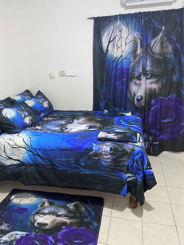 A bedroom with a bed covered in a wolf-themed duvet, a large wolf tapestry on the wall, and a wolf-themed rug.