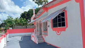 A building with a red and white facade, a gated entrance, and a staircase leading to a door. - Family Reunions Holiday 4 Bedrooms, 5 Beds Rentals in St Thomas,jamaica (Port Morant)