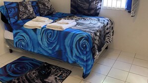 A bedroom with a bed covered in blue floral bedding, a window with a decorative curtain, and a matching rug on the floor. - Family Reunions Holiday 4 Bedrooms, 5 Beds Rentals in St Thomas,jamaica (Port Morant)