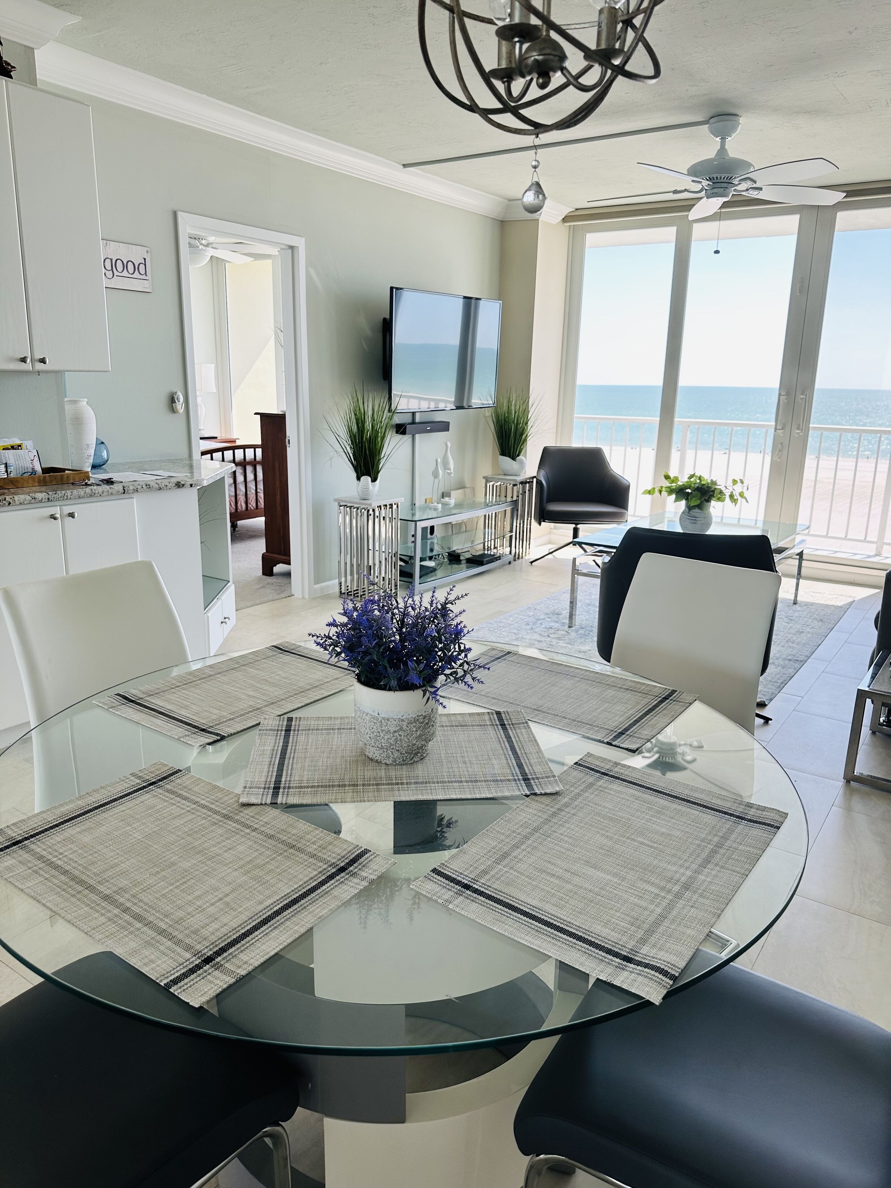 Una cocina moderna con armarios blancos, un comedor con mesa de vidrio y vista al océano.