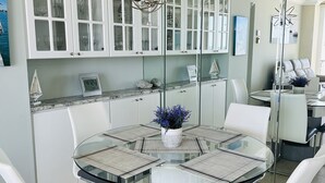 A modern dining area with a glass table, white chairs, and a decorative centerpiece. - Wake up to the sound of waves and panoramic Gulf views at this beachfront condo  (Marco Island)
