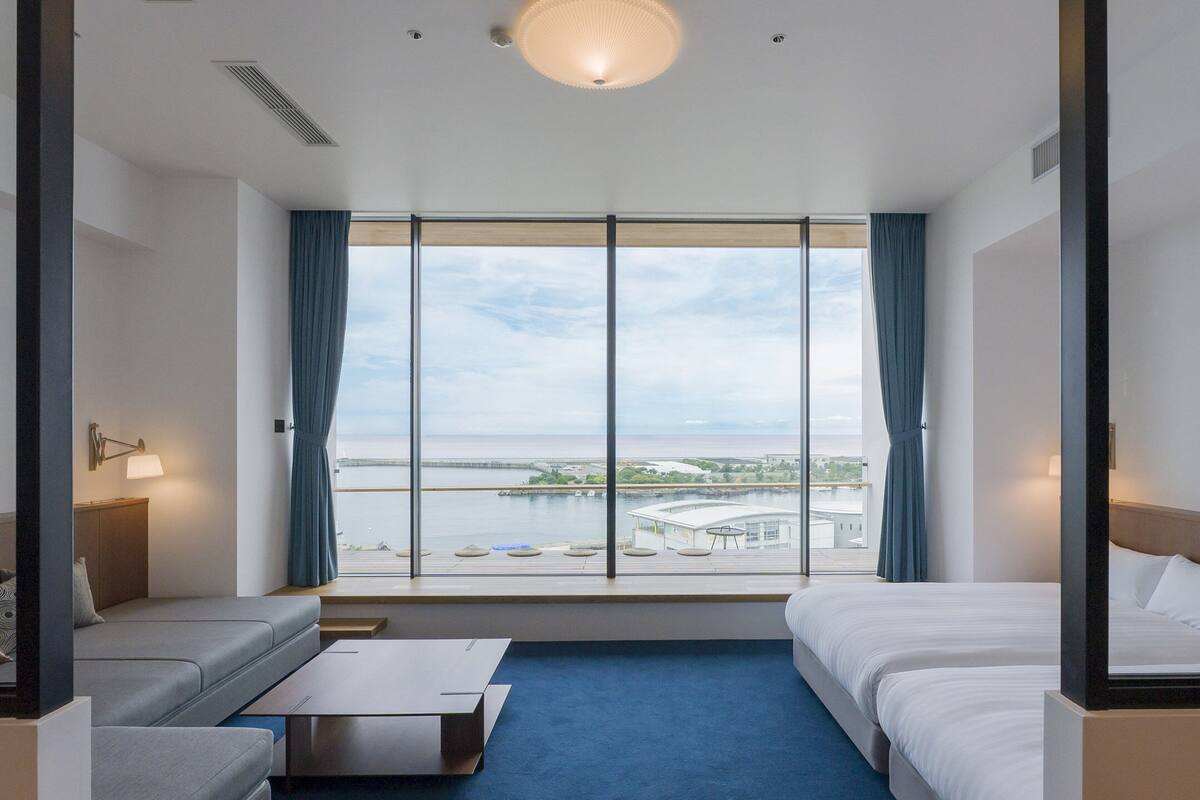 Habitació d'hotel amb una finestra gran, un llit, un sofà i una taula petita.