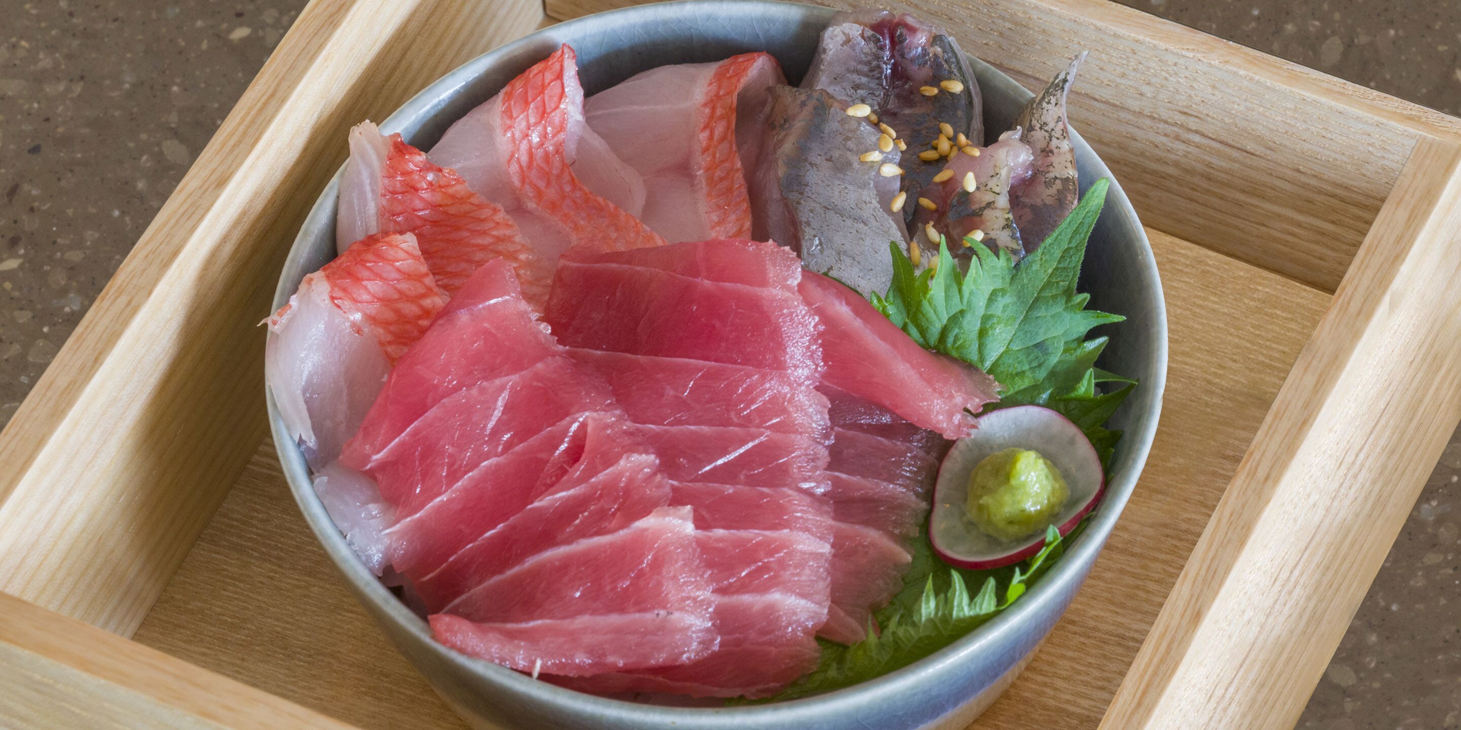 A bowl of sashimi with various fish slices, garnished with sesame seeds and a small green garnish.