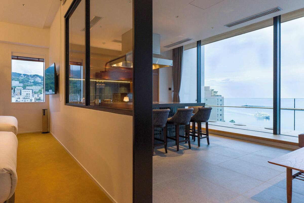 Habitació d'hotel amb dos llits, un balcó que ofereix vistes a la ciutat i una zona de bar amb seients.