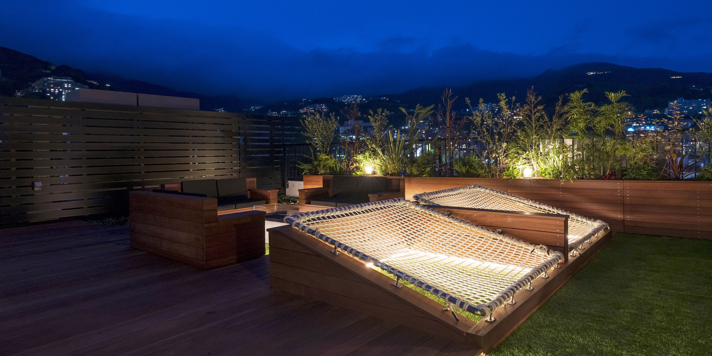 A rooftop terrace with a hammock, seating area, and a view of a cityscape at night.