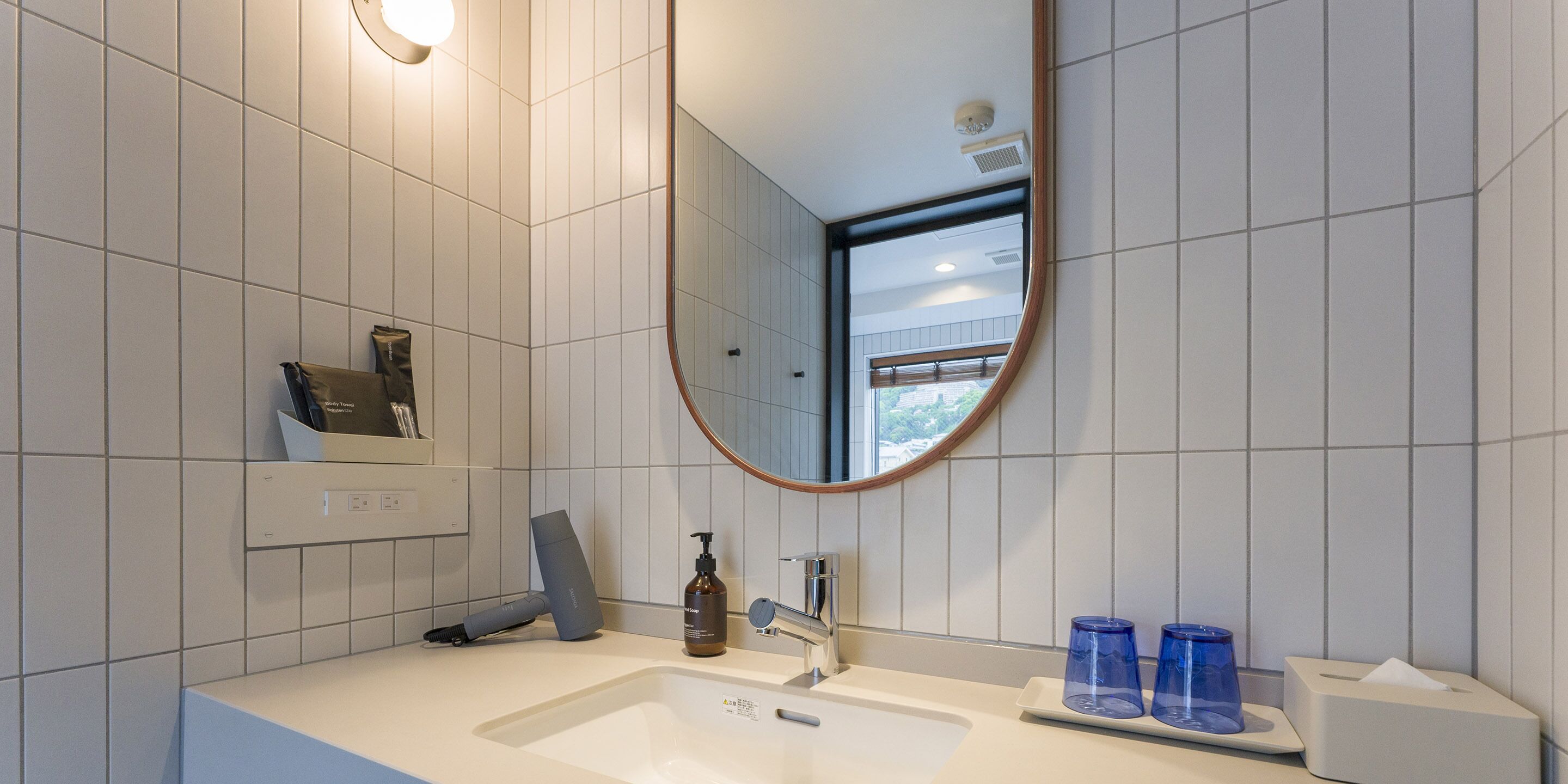 Un baño moderno con un lavamanos blanco, un espejo y una ventana.
