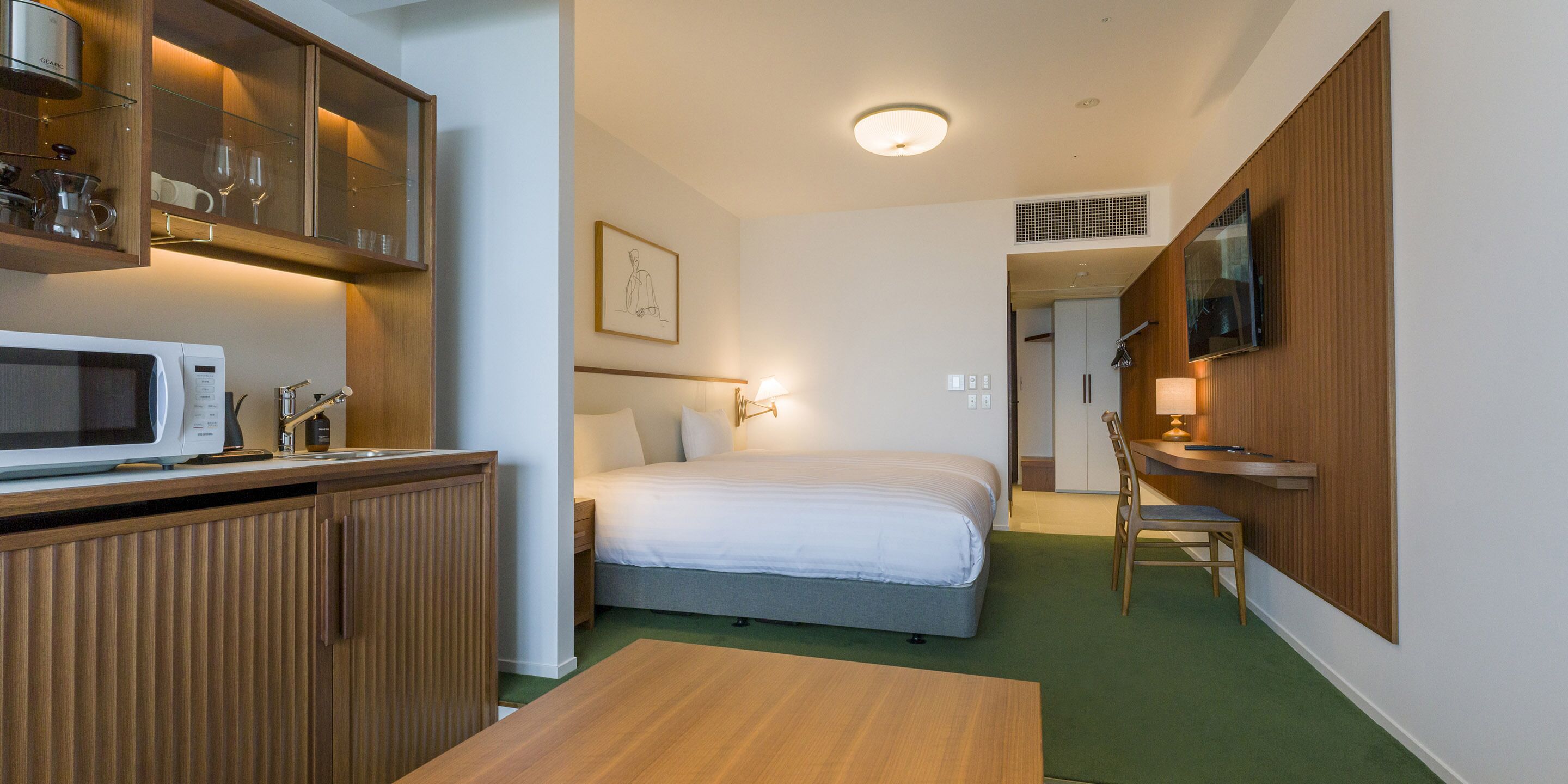 A compact hotel room with a kitchenette, a bed, a desk, and a television.
