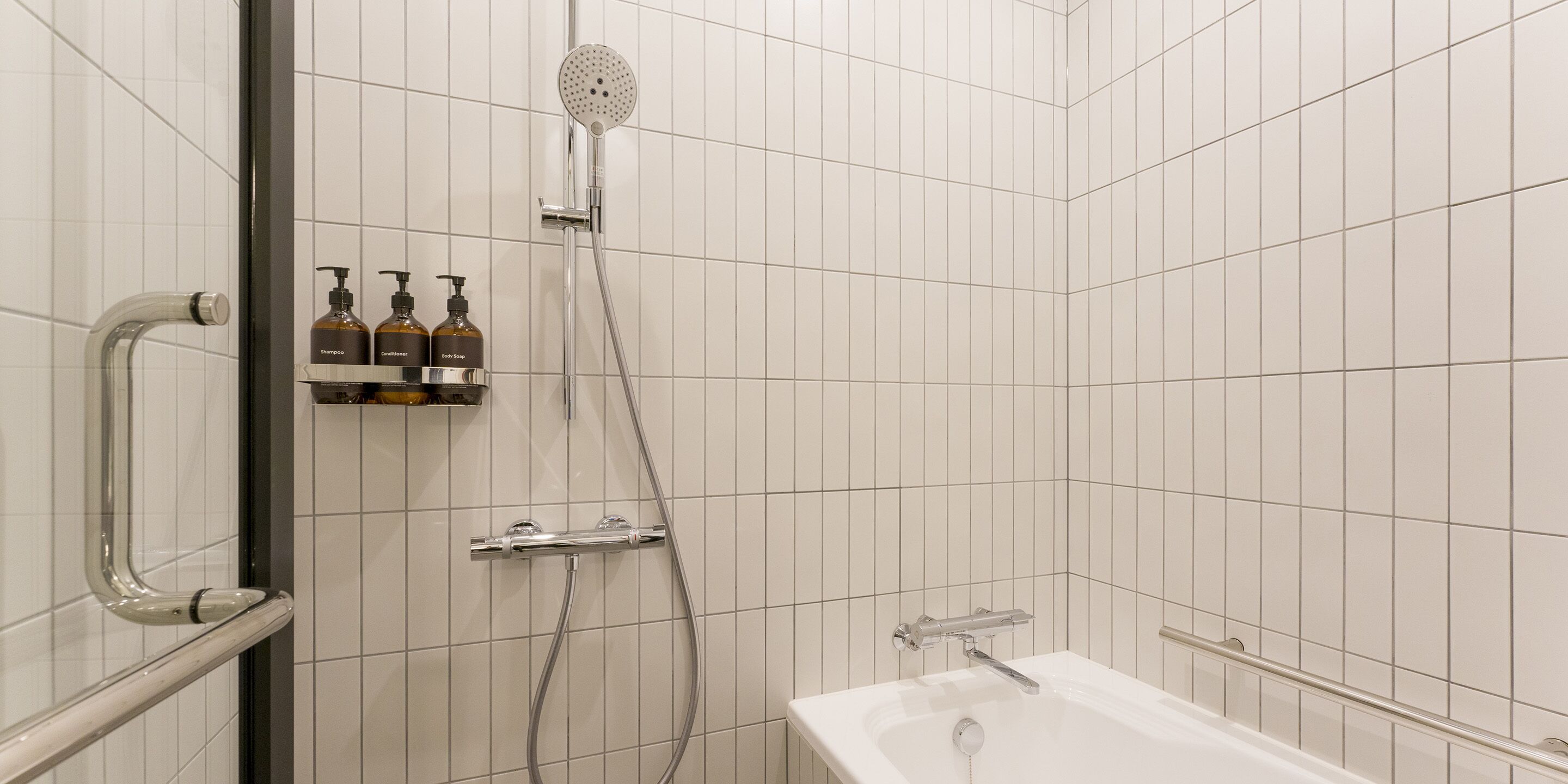 A modern bathroom with a shower, a bathtub, and a shelf with three bottles of shampoo, conditioner, and body wash.