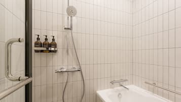 Un baño moderno con ducha, bañera y repisa con tres botellas de champú, acondicionador y gel de baño.
