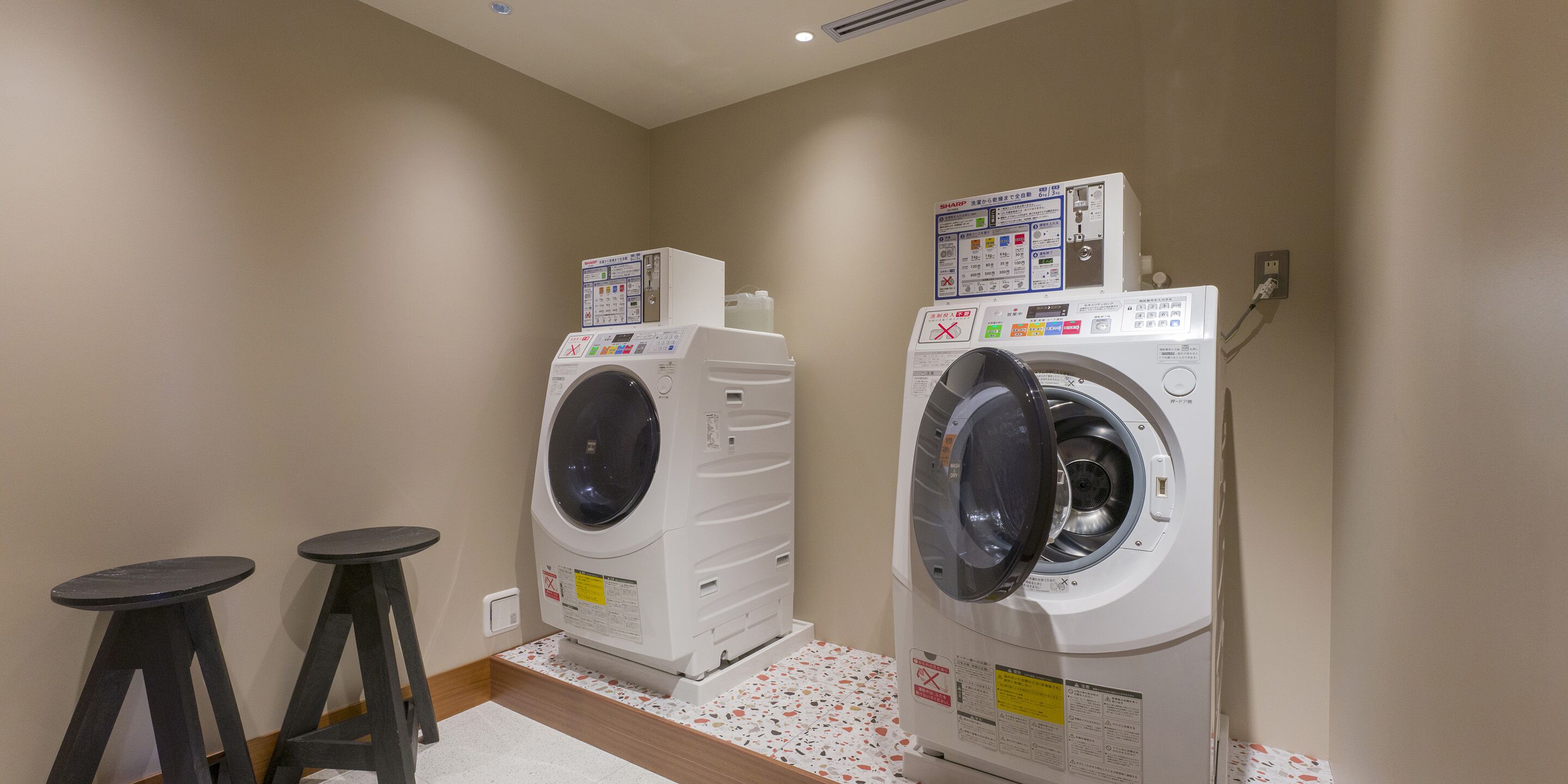 A laundry room with two stacked washers and dryers, a small table, and a stool.