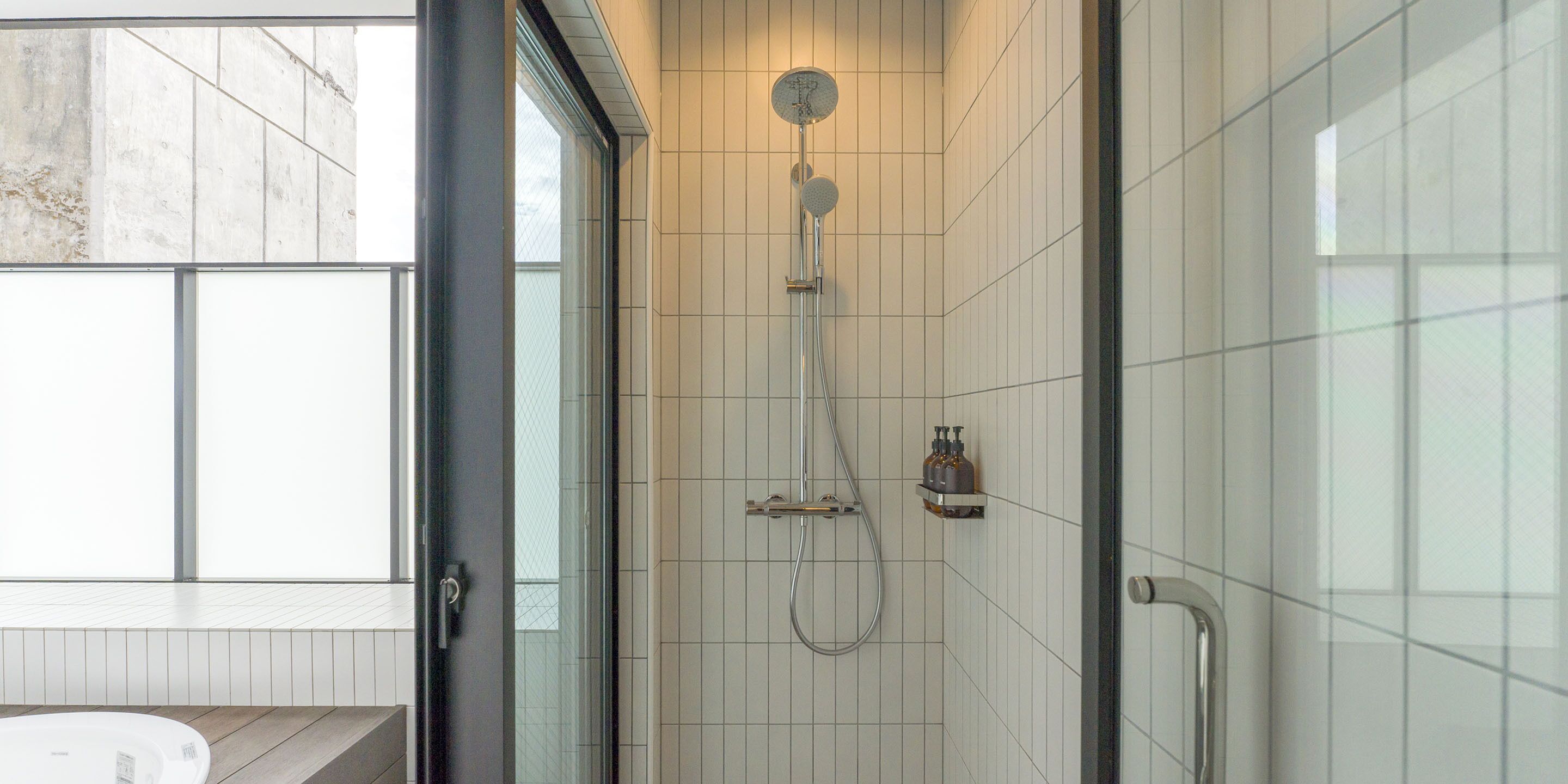 A modern bathroom with a glass-enclosed shower, white tiled walls, and a wooden floor.