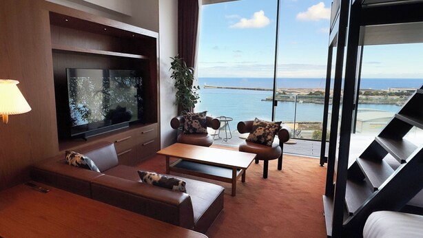 Ein modernes Wohnzimmer mit großem Fernseher, bequemen Sitzmöglichkeiten, einer Pflanze und Meerblick.