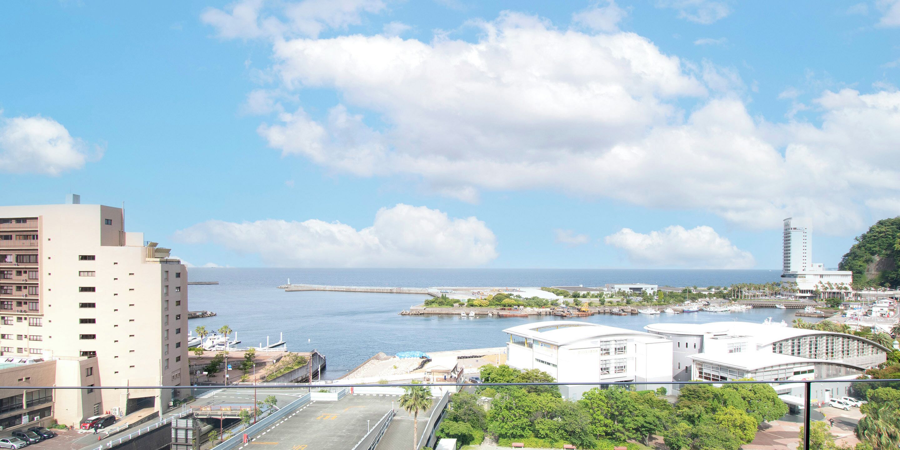 A coastal cityscape with a prominent high-rise building, a marina, and a bridge.