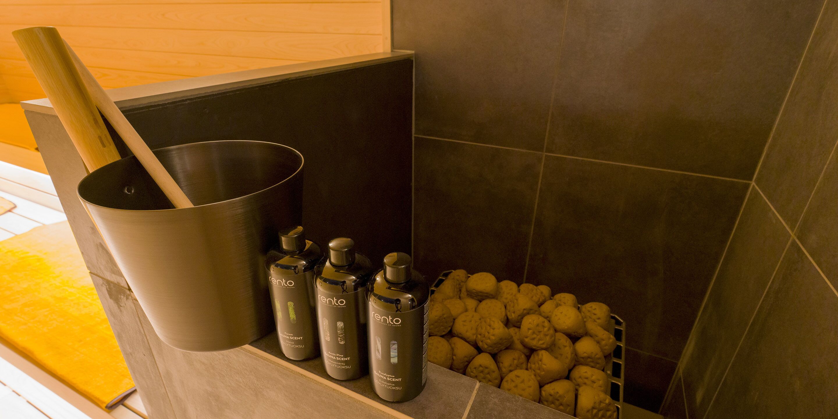 Ein Badezimmer mit einer schwarzen Badewanne, einer Holzbadematte und drei Flaschen Rento Duschgel.