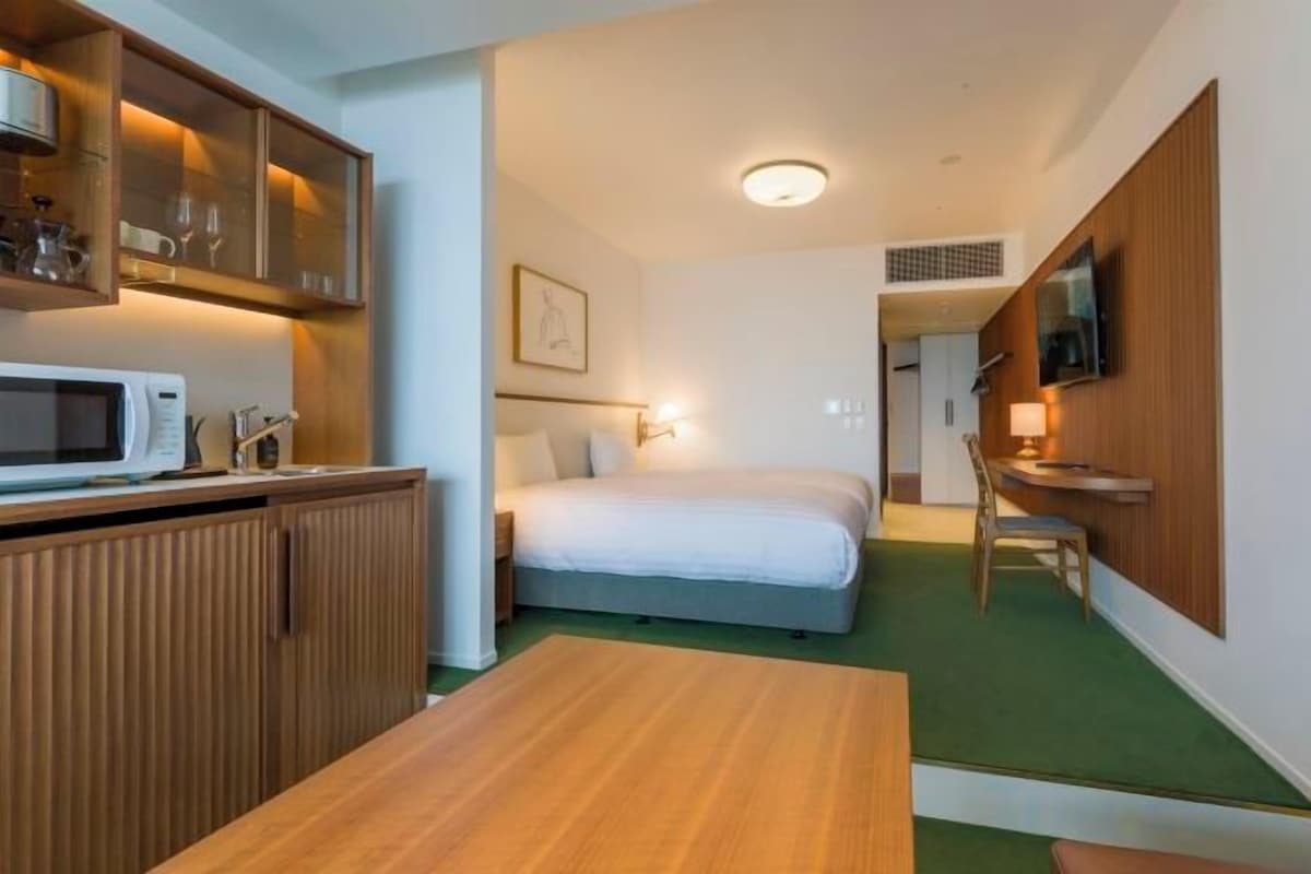 A compact hotel room with a bed, a desk, a microwave, and a TV.