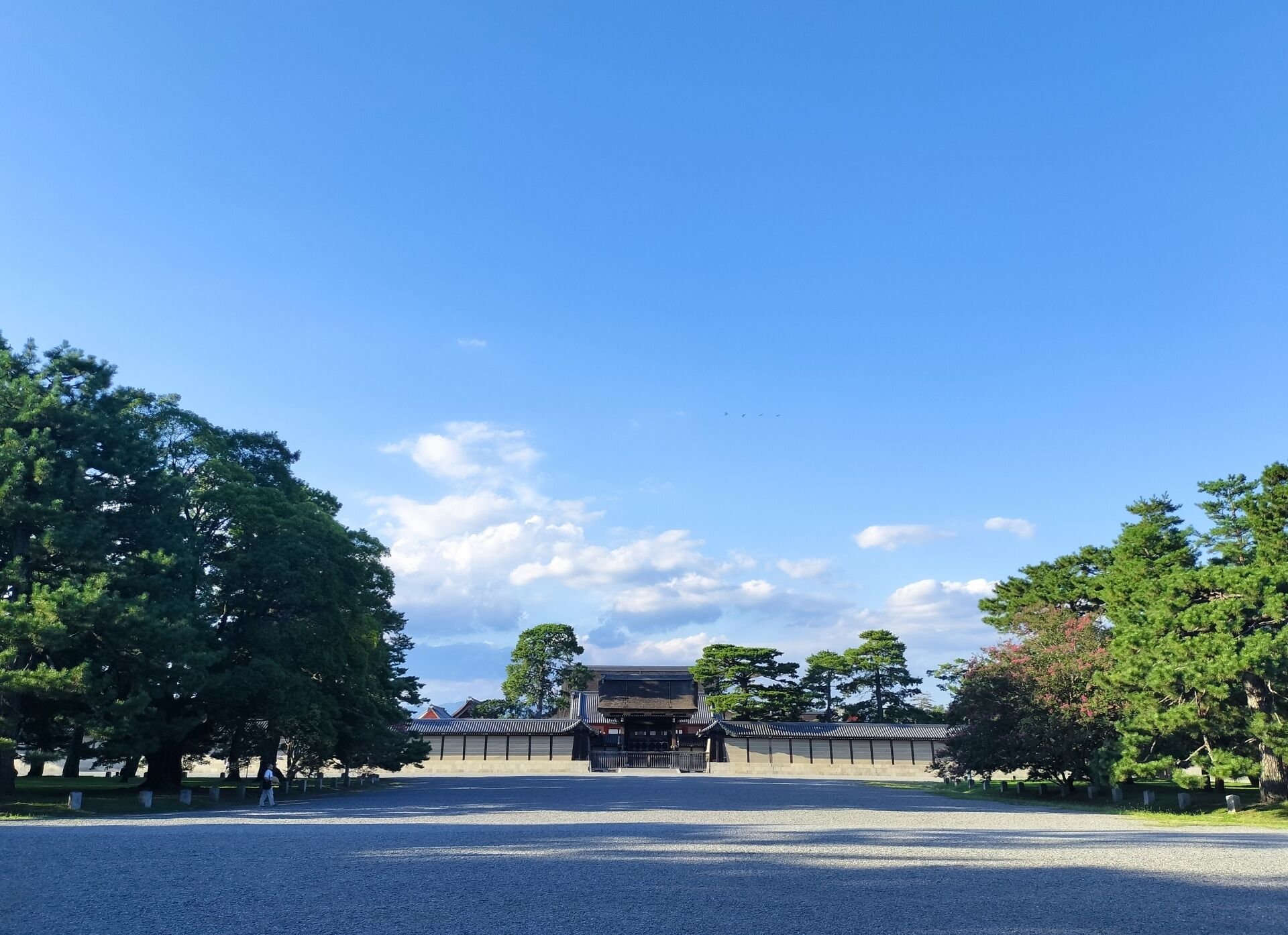 A traditional Japanese building with a central entrance, surrounded by trees and a gravel path.