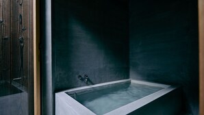 Ein modernes Badezimmer mit einer freistehenden Badewanne, einer Duschkabine aus Glas und einer dunkel, strukturierten Wand.