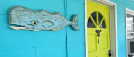 Un bâtiment turquoise avec une porte jaune vif et une décoration en forme de poisson en bois sur le mur.