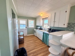 A compact kitchen with white cabinets, a stove, a sink, and a window with blinds.