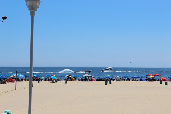 Une plage avec des tentes et des parasols, un jet ski et un bateau sur l’eau.